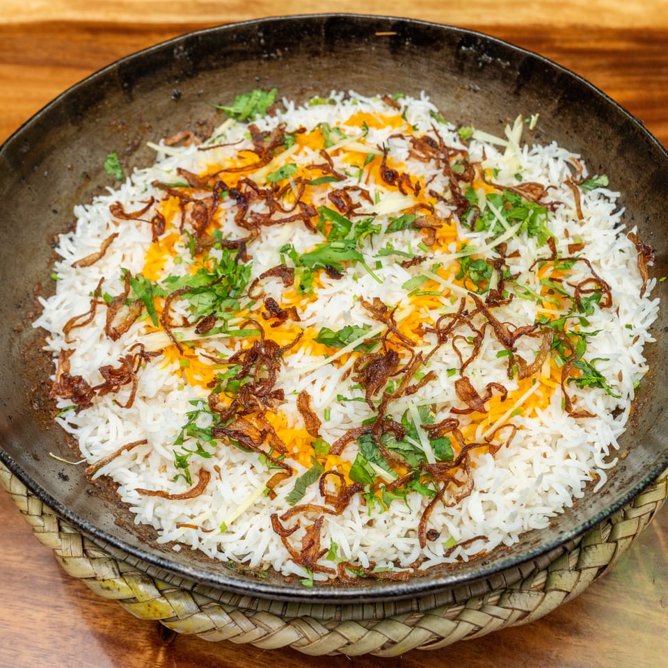 Fragrant basmati rice layered with saffron, fried onions, ginger, and fresh cilantro in a black serving pan.