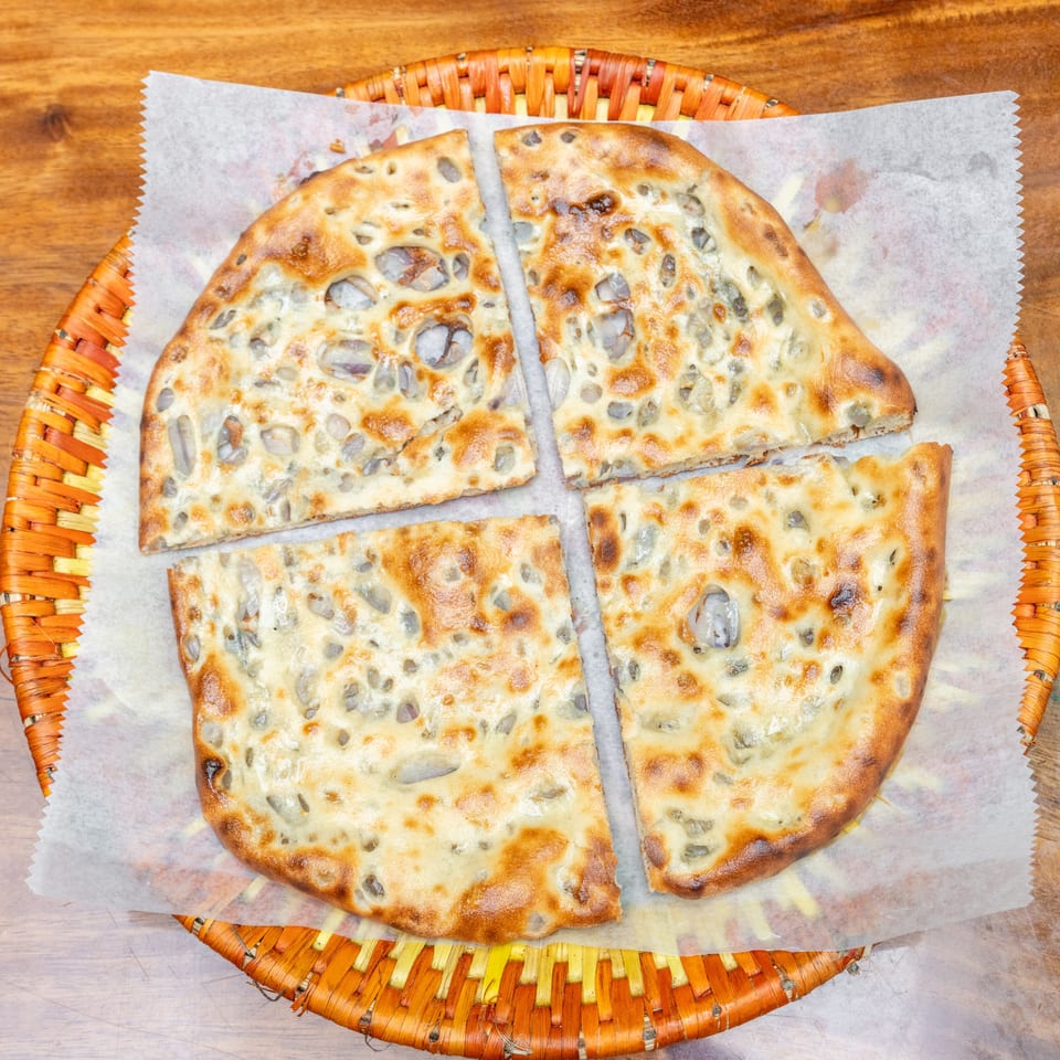 Four pieces of golden, herb-studded flatbread arranged in a woven basket on a wooden table.